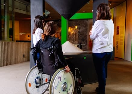 Person im Rohlstuhl vor Sanduhr in barrierefreier Ausstellung