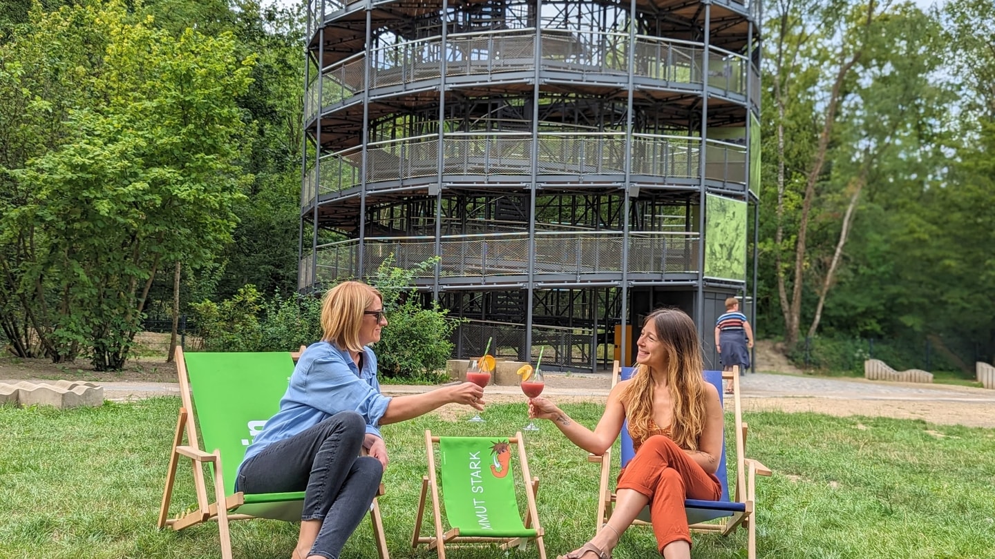 Erwachsene auf Liegestühlen mit Cocktail aus Gastronomie vor Erlebnisturm Höhlenblick