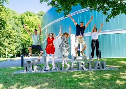 Erwachsene springen vom Neandertal Schriftzug vor dem Neanderthal Museum