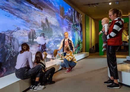 Familie betastet Knochen und Mammutzahn vor Klimawand in Ausstellung
