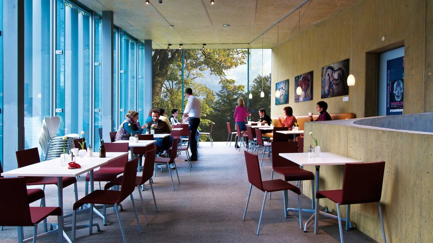 Besuchende sitzen im Museumscafe vor großen Fensterscheiben