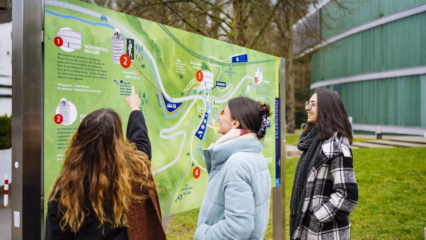 Drei Frauen stehen vor einer Übersichtskarte der Erlebniswelt Neandertal